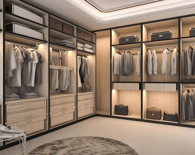 Vestidor con estantes empotrados, cajones y barras para colgar lleno de ropa, iluminado con una luz suave.