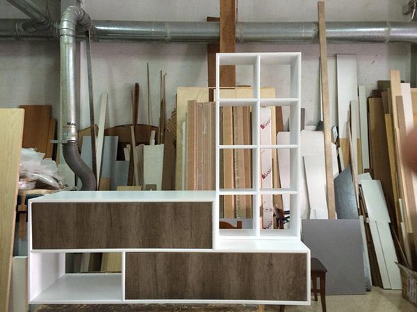 Mueble de almacenaje blanco con vetas de madera en un taller de carpintería. El mueble cuenta con estantería, cajones y estantes abiertos.