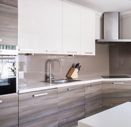 Cocina moderna con gabinetes blancos y con vetas de madera, electrodomésticos de acero inoxidable y un protector contra salpicaduras gris claro.
