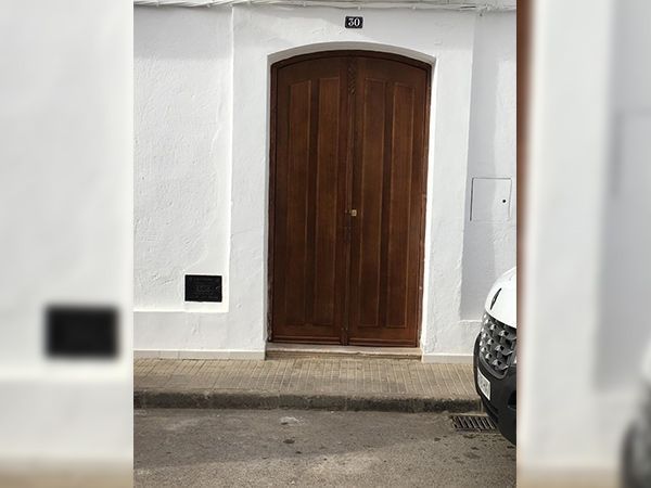 Puerta doble de madera situada en pared blanca, con una pequeña caja negra a la izquierda y el frente de un automóvil a la derecha.