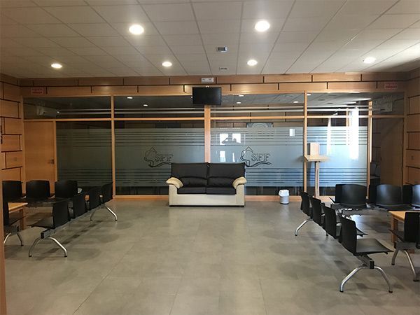 Una sala de espera con un sofá negro, sillas negras y paredes de vidrio con diseño esmerilado.