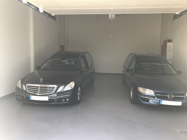Dos coches fúnebres negros aparcados en un garaje vacío y luminoso. Los coches miran hacia delante, uno al lado del otro.