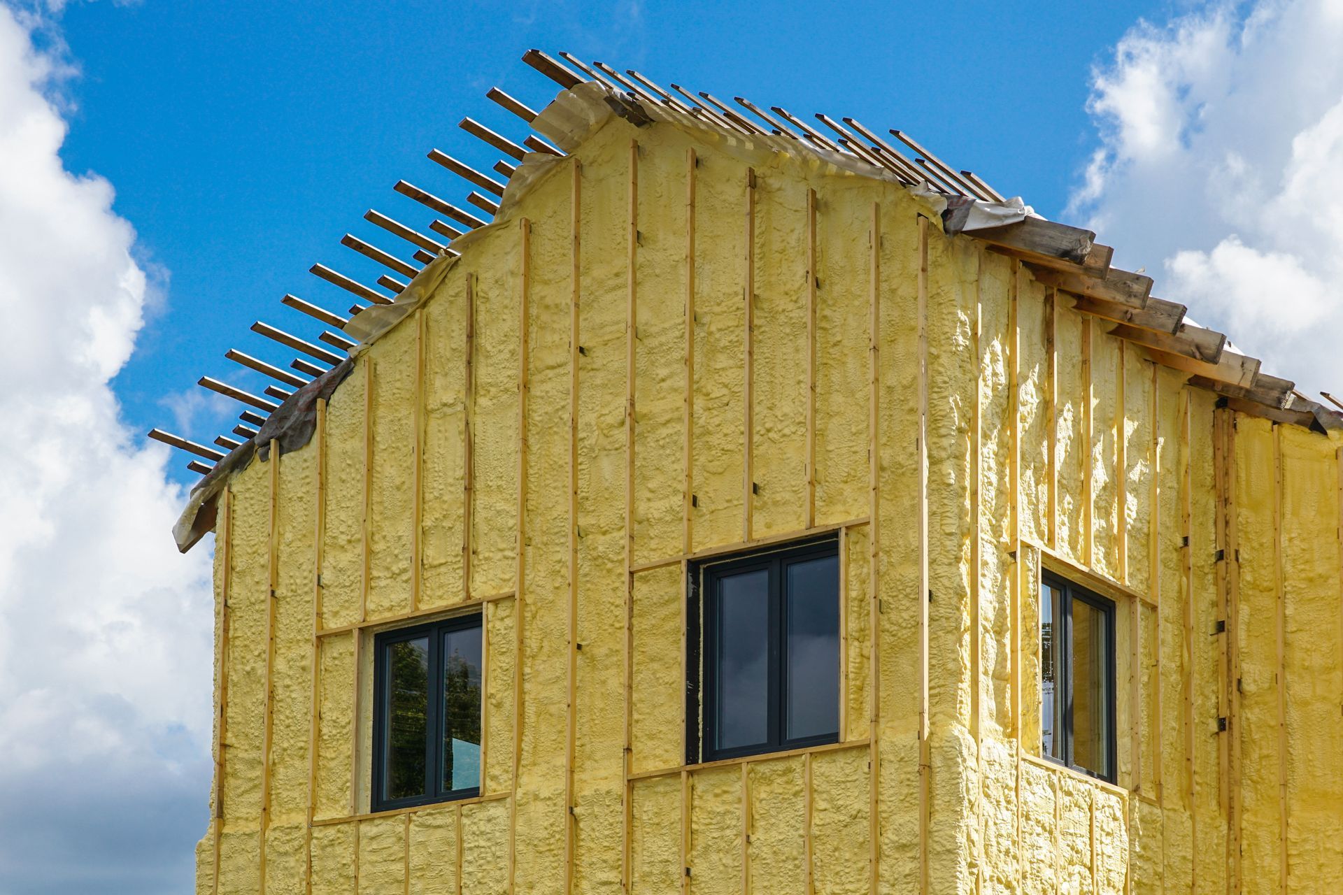 Maison en construction avec isolation jaune, fenêtres sombres et ciel bleu. Lien vers la page isolation extérieure.