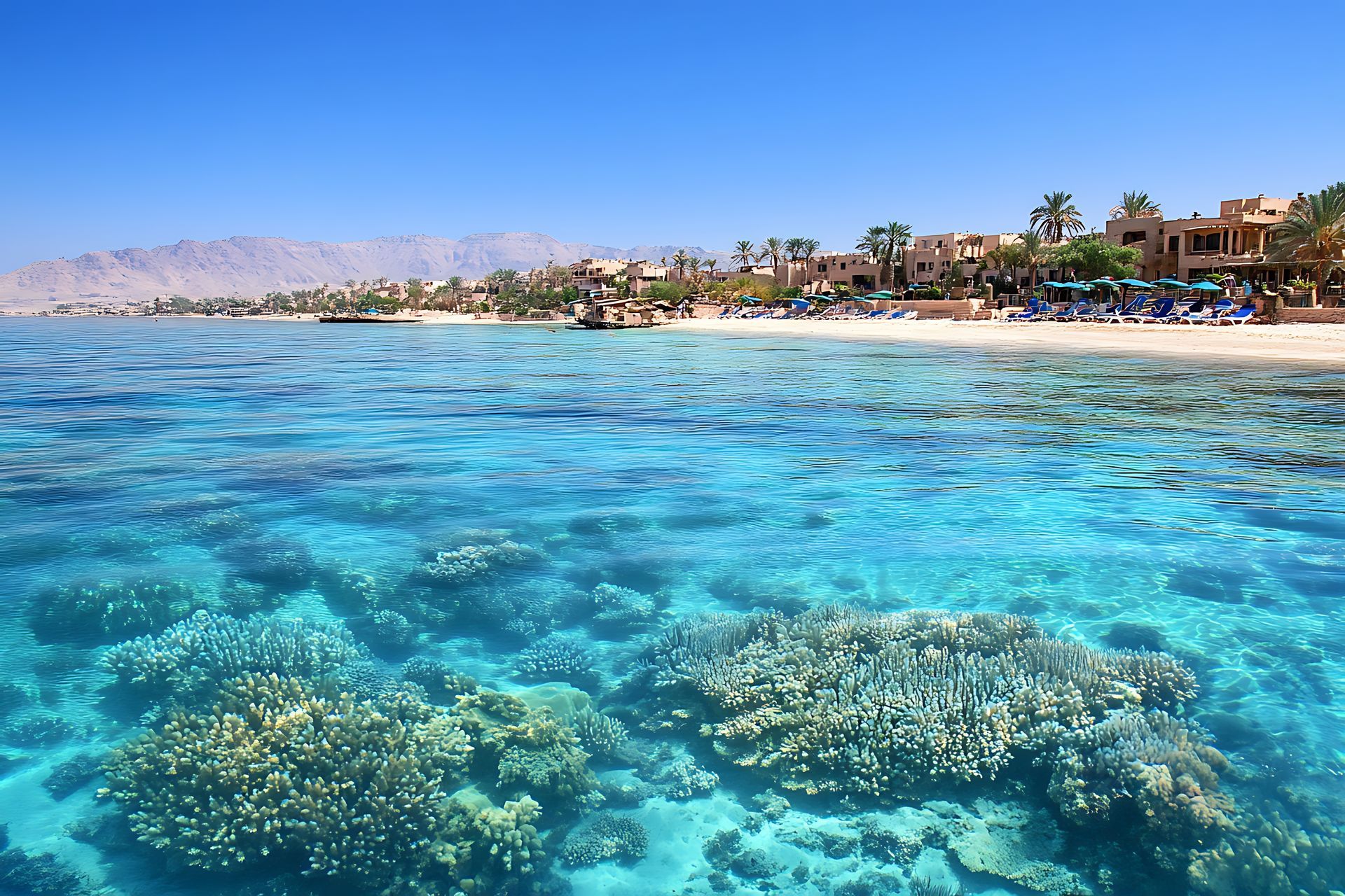 Récif corallien turquoise dans une mer claire et peu profonde, avec une plage de sable et des complexes hôteliers le long du rivage.