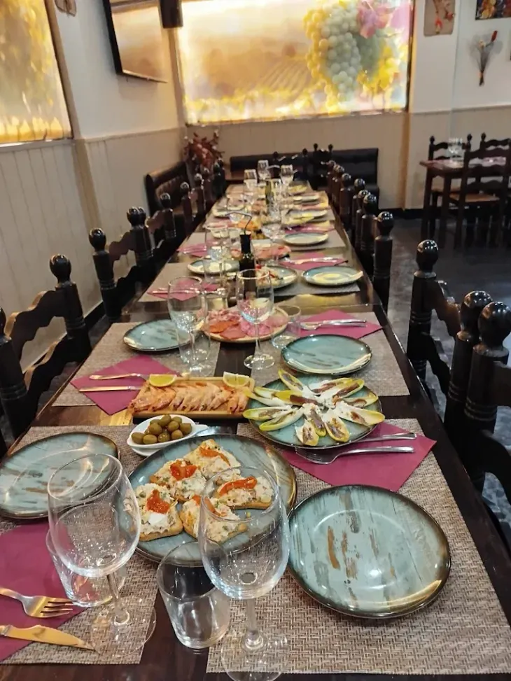 Una larga mesa de comedor puesta con platos, vasos y aperitivos en el comedor de un restaurante con iluminación cálida.