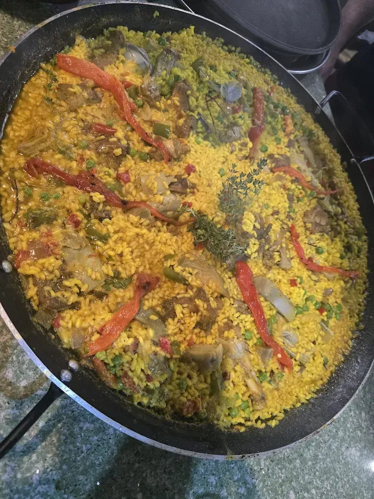 Sartén de arroz amarillo cubierta con hierbas verdes y chiles rojos, cocinándose en la estufa.