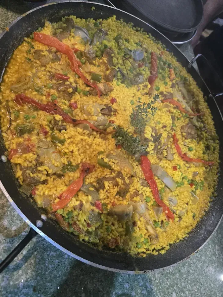 Sartén de arroz amarillo cubierta con hierbas verdes y chiles rojos, cocinándose en la estufa.