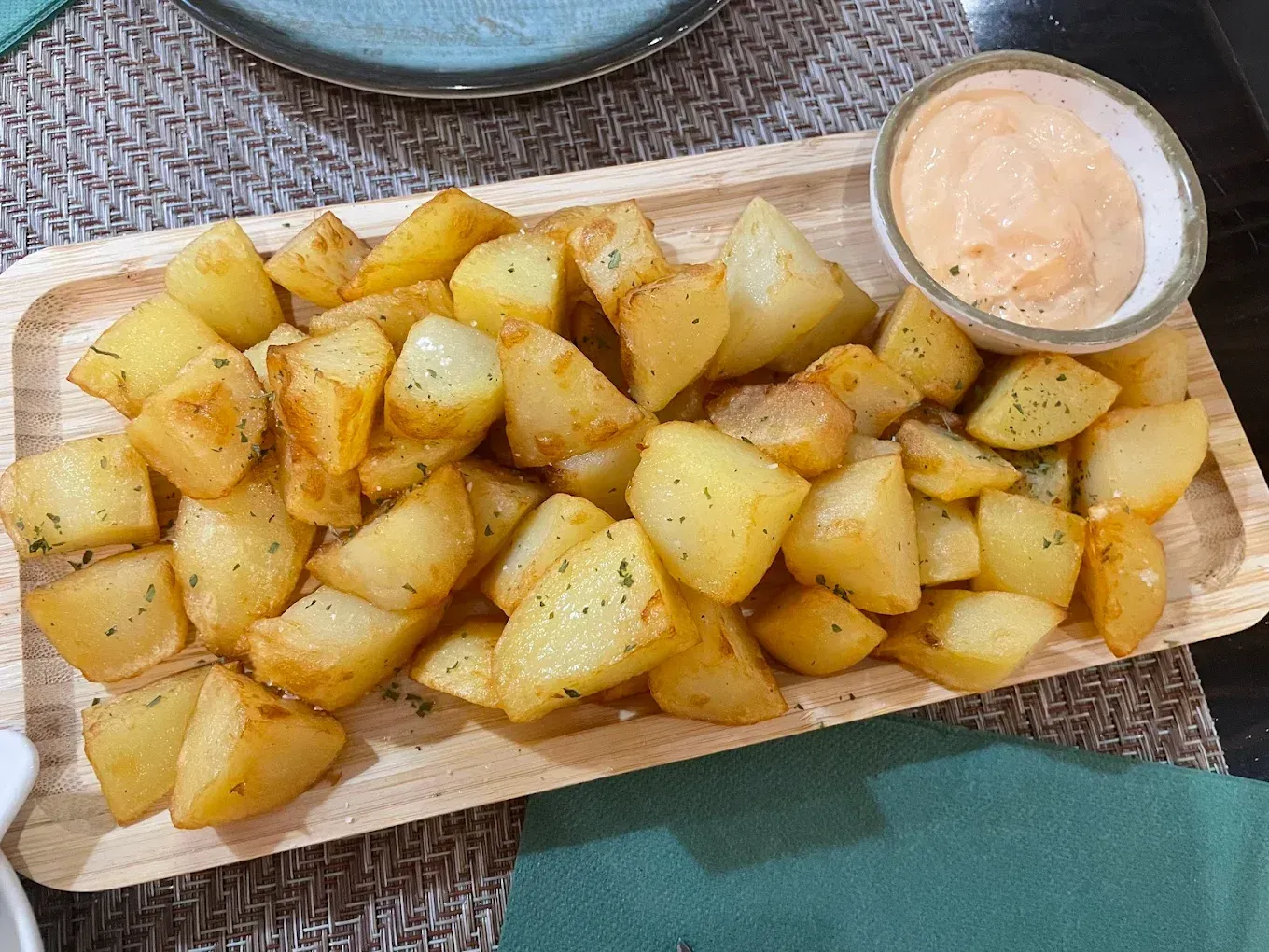 Bandeja de patatas gajo sazonadas con salsa para mojar sobre una tabla de madera.
