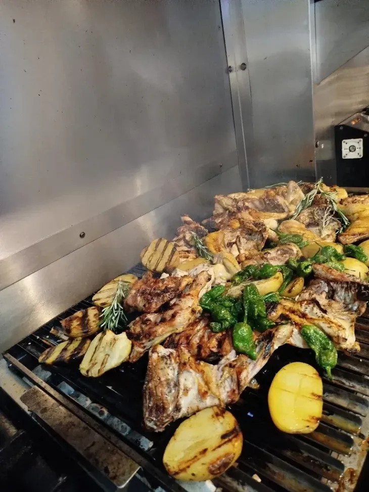 Verduras y carne a la parrilla cocinándose en una barbacoa, con calabaza amarilla chamuscada en primer plano.