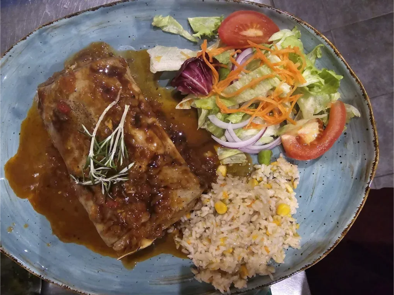 Filete a la parrilla con salsa, arroz y ensalada mixta en un plato azul.