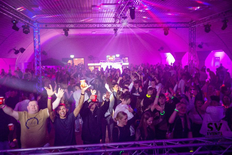 Eine große Menschenmenge tanzt in einem Club mit violetten Lichtern.