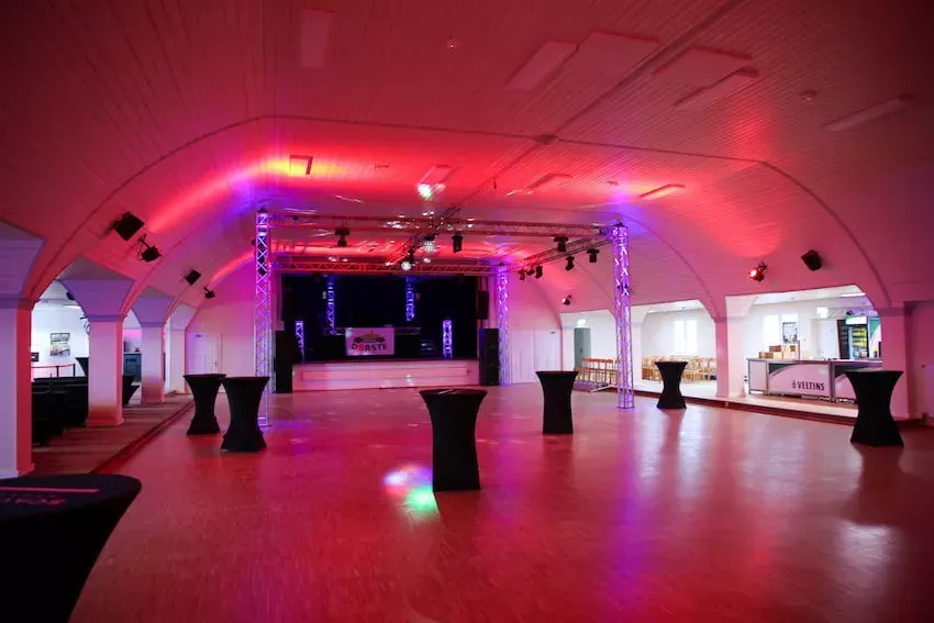 Ein großer leerer Raum mit Tischen und einer Bühne.