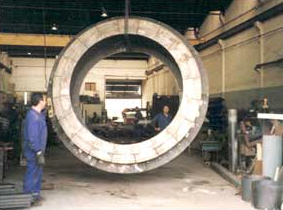 Un hombre está parado frente a un gran anillo de metal en una fábrica.