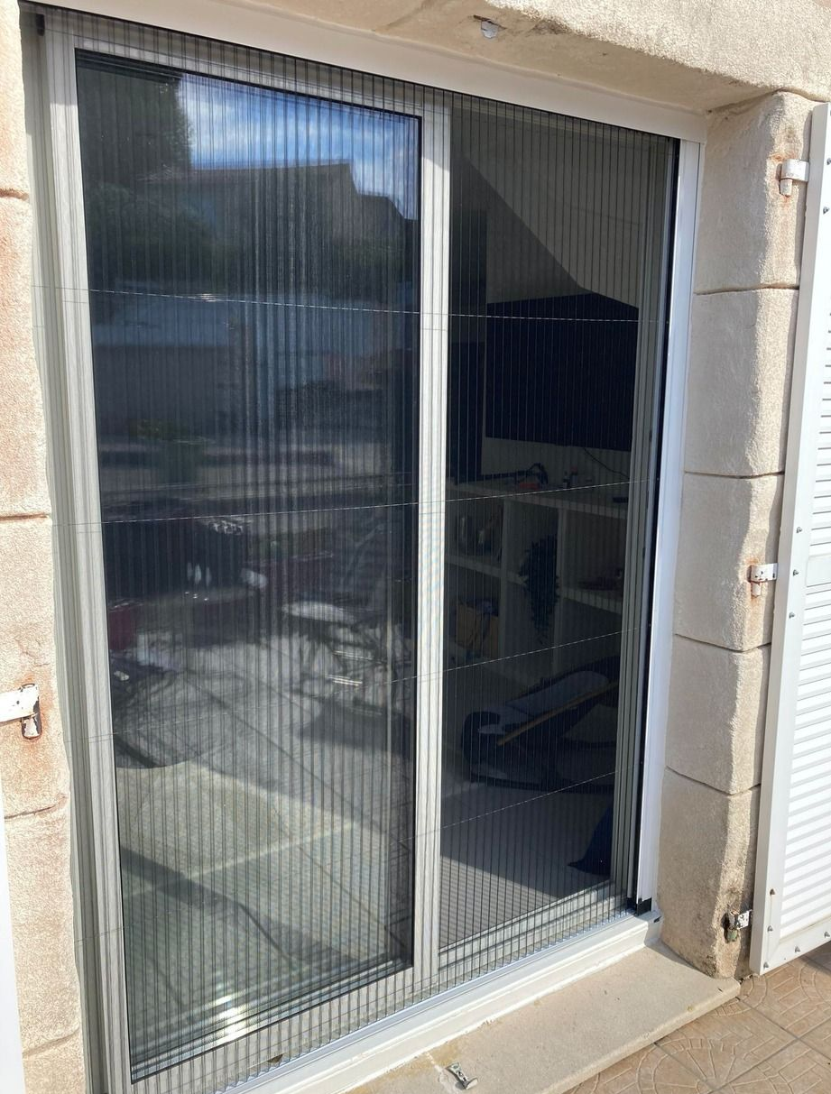 Porte moustiquaire coulissante, fermée, dans un cadre blanc, avec vue à l'intérieur d'une pièce.