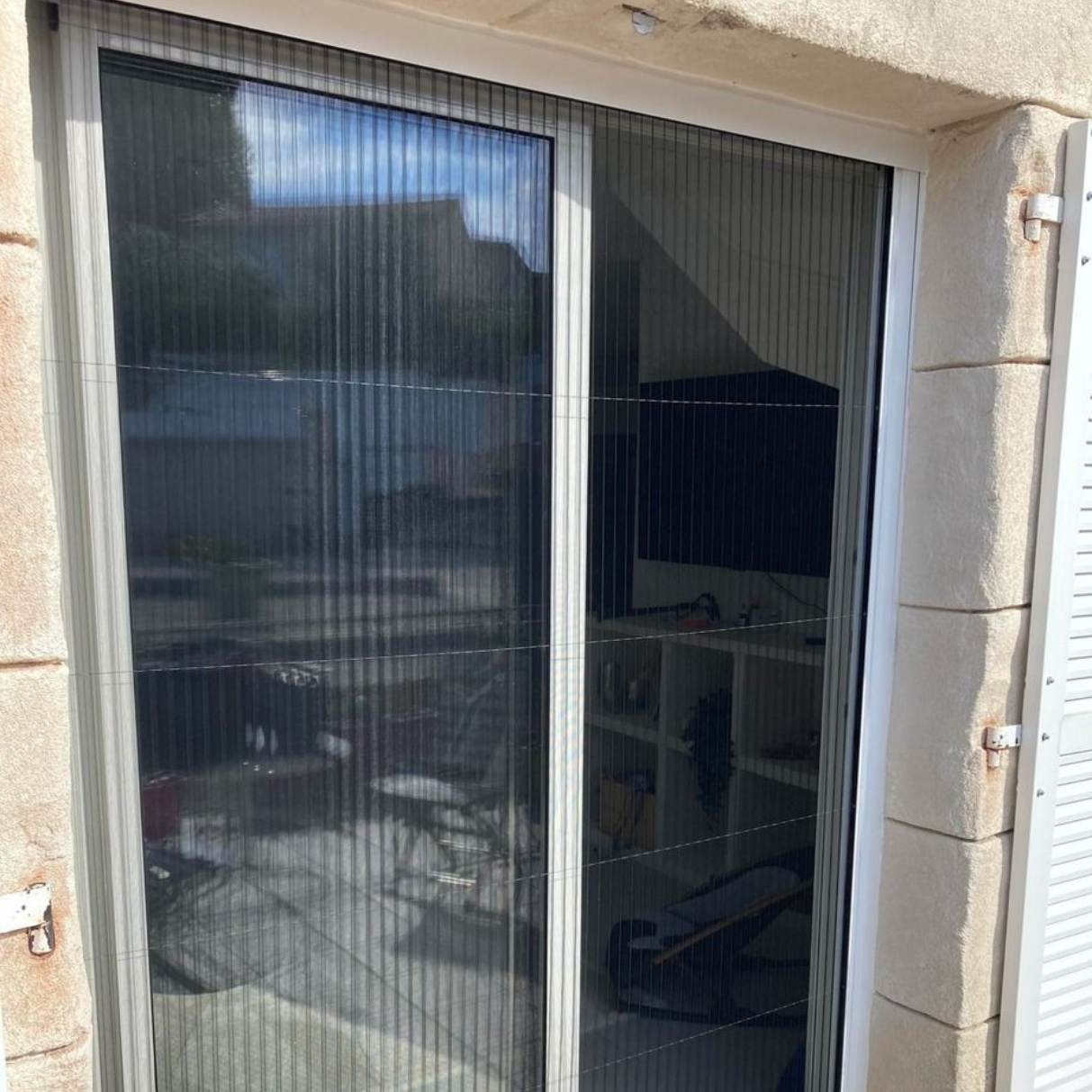 Porte coulissante en verre avec moustiquaire rétractable noire, vue extérieure d'un bâtiment.