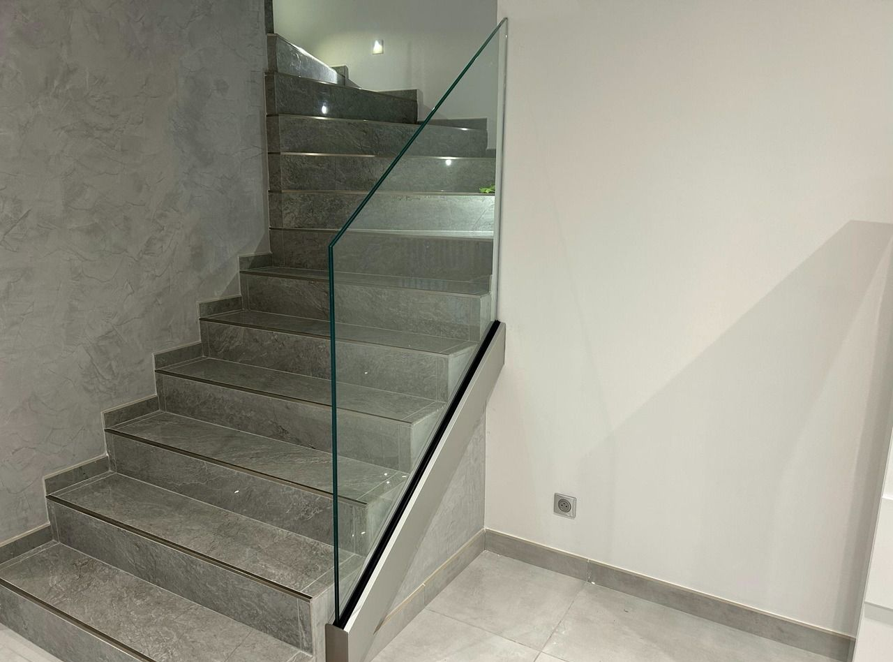 Escalier en carrelage gris avec garde-corps en verre.