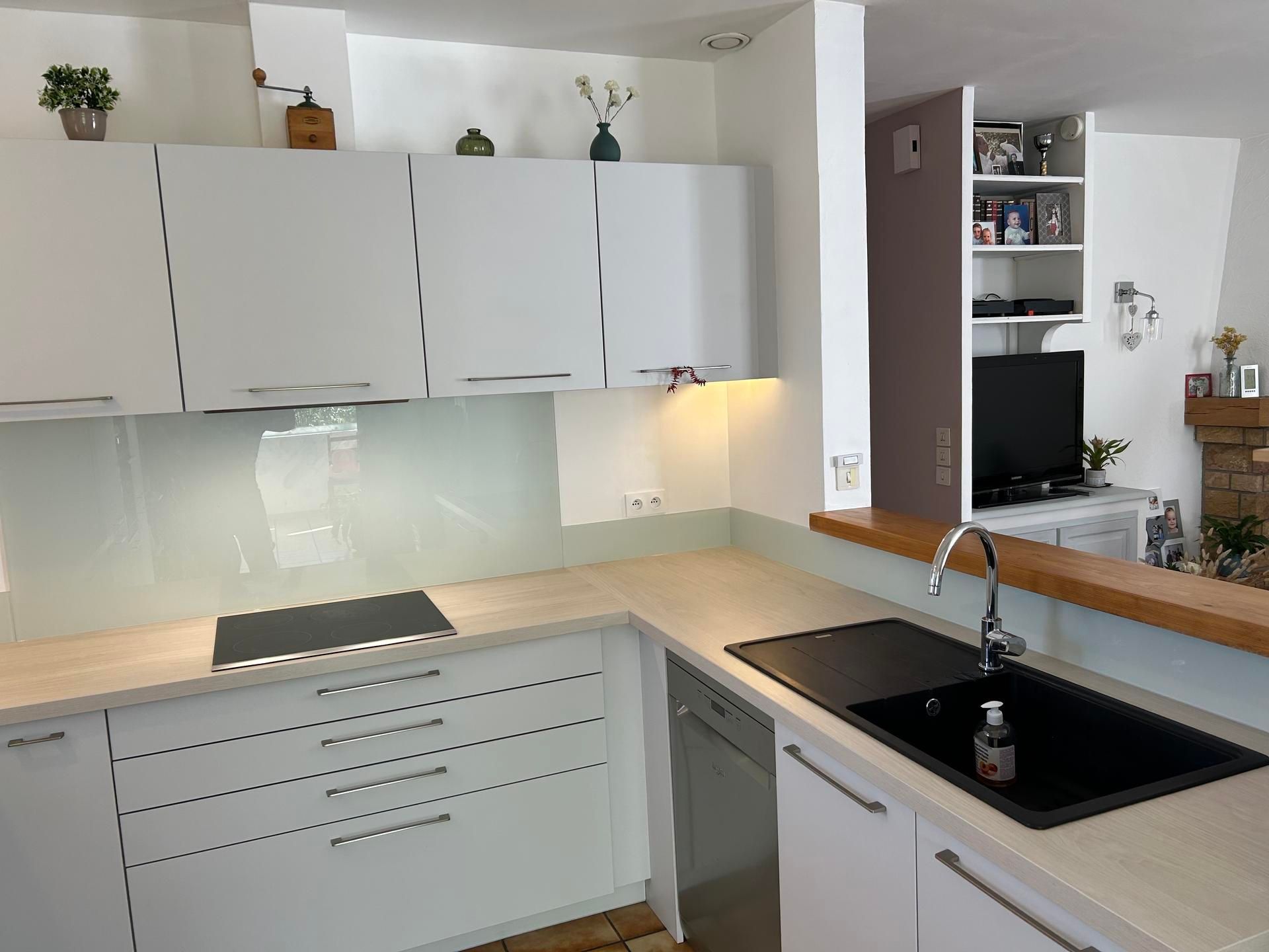 Cuisine blanche avec comptoirs clairs et évier noir. Meubles hauts décorés.