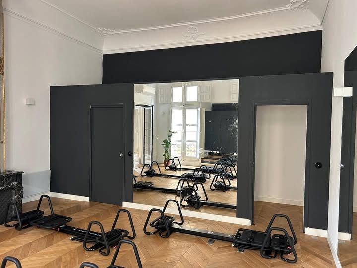 Intérieur de salle de sport avec machines d'exercice, grand miroir et panneaux muraux noirs.