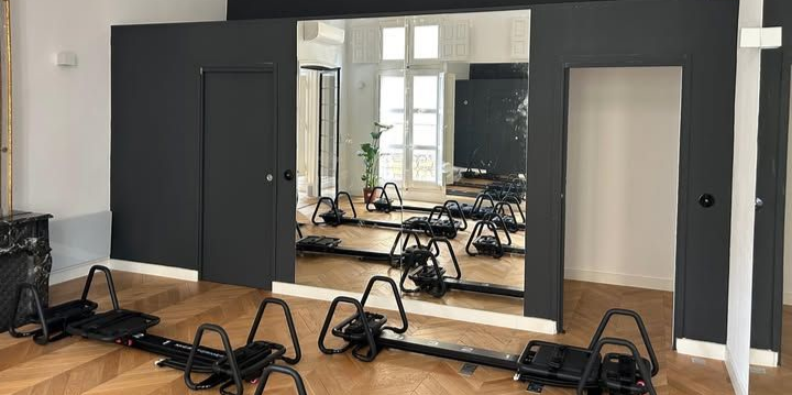 Salle de sport intérieure avec appareils de musculation et grand miroir. Murs gris foncé et parquet.