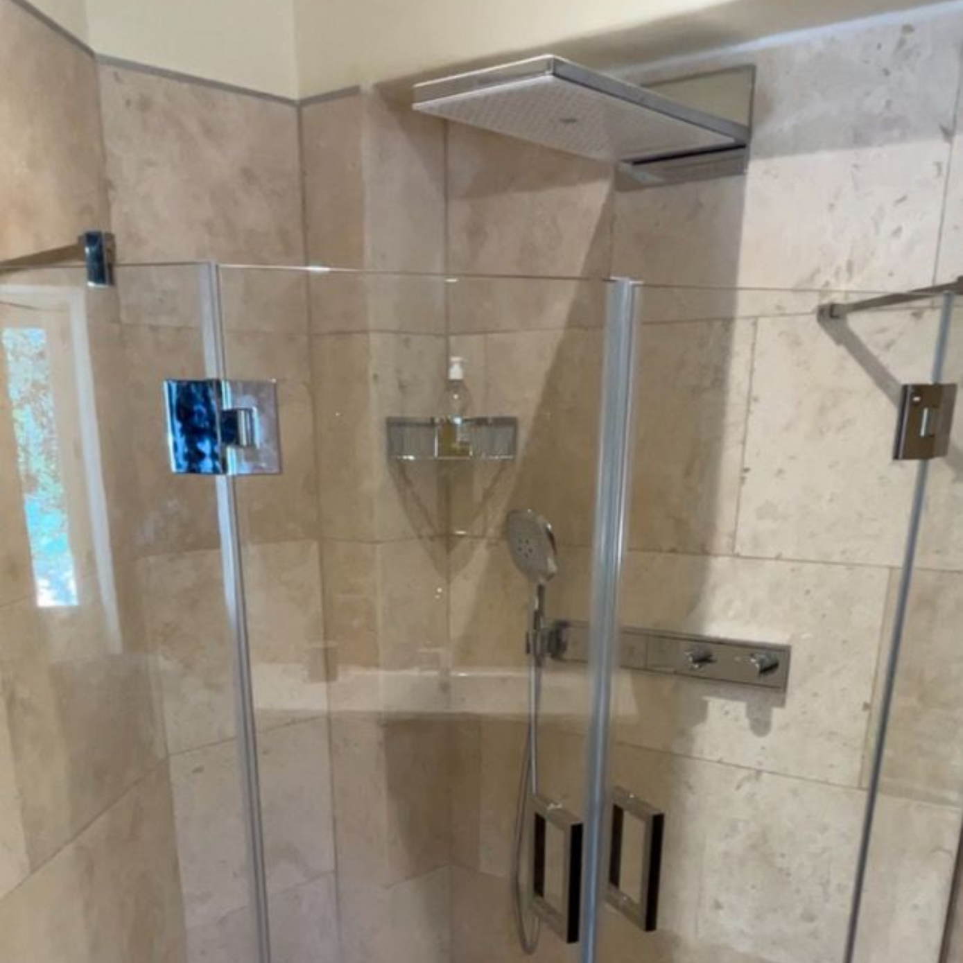 Une douche moderne avec des portes en verre et des accessoires chromés, sur du carrelage de couleur claire.