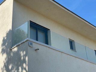 Extérieur d'un bâtiment moderne avec une balustrade de balcon en verre et une petite fenêtre.
