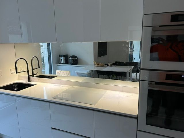 Cuisine moderne avec armoires blanches, comptoir en marbre, luminaires noirs et dosseret en miroir.