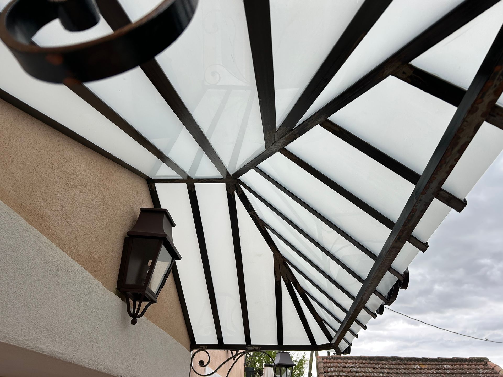 Vue extérieure d'un auvent avec un toit blanc et des poutres de soutien sombres au-dessus d'une porte.