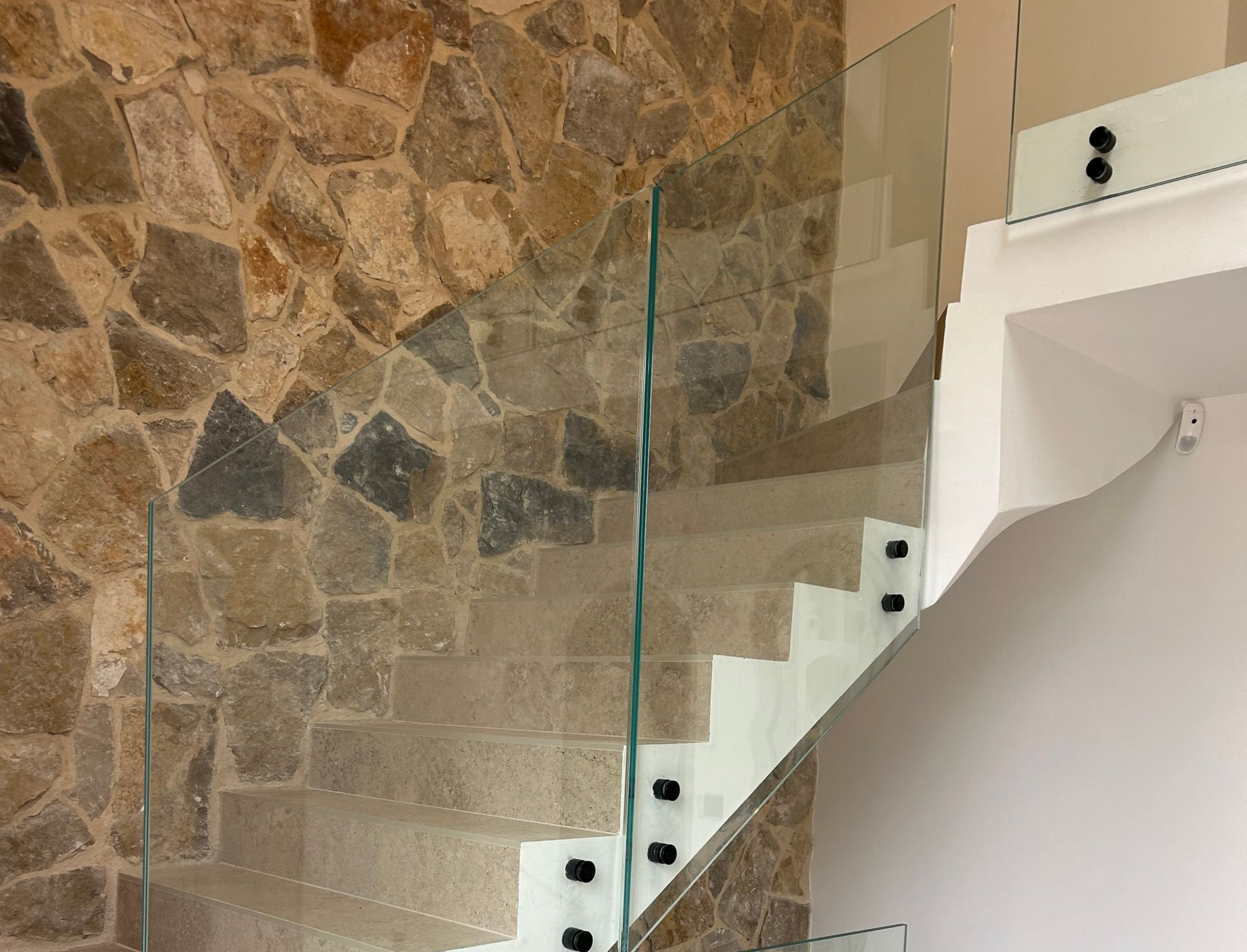 Escalier avec garde-corps en verre et mur en pierre.