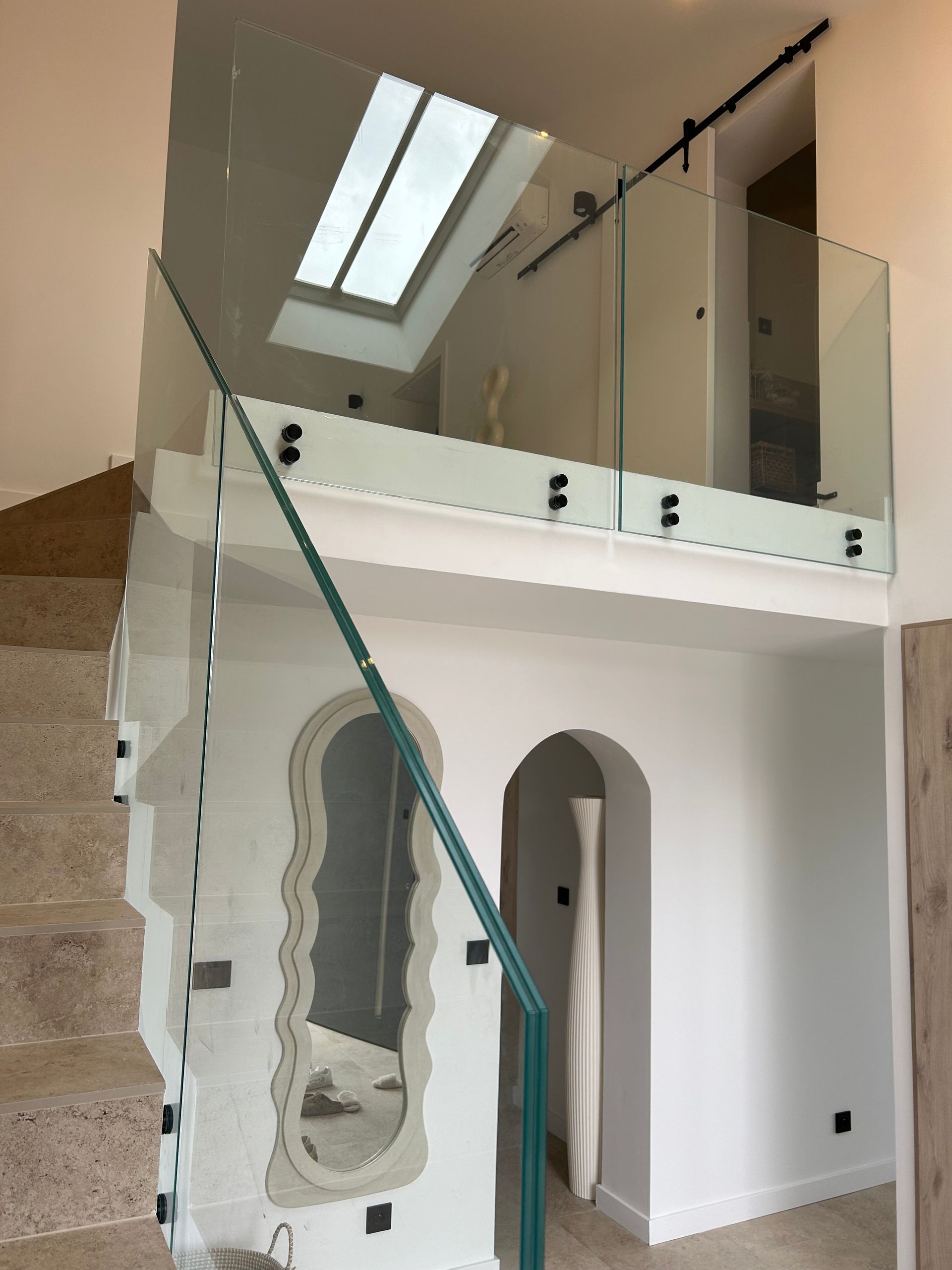 Escalier en verre avec garde-corps et balcon au deuxième étage, lumière naturelle provenant du puits de lumière.