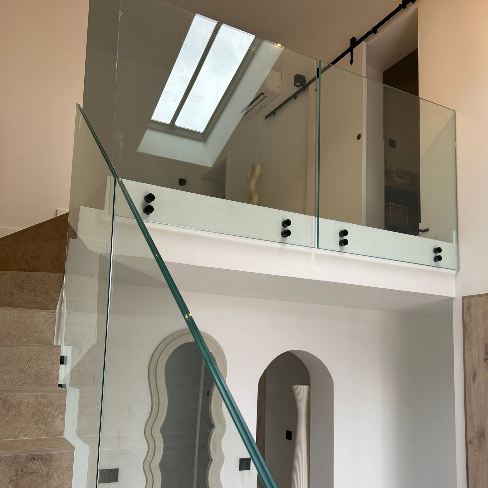 Escalier en verre avec garde-corps en verre. Murs blancs, puits de lumière et quincaillerie noire.