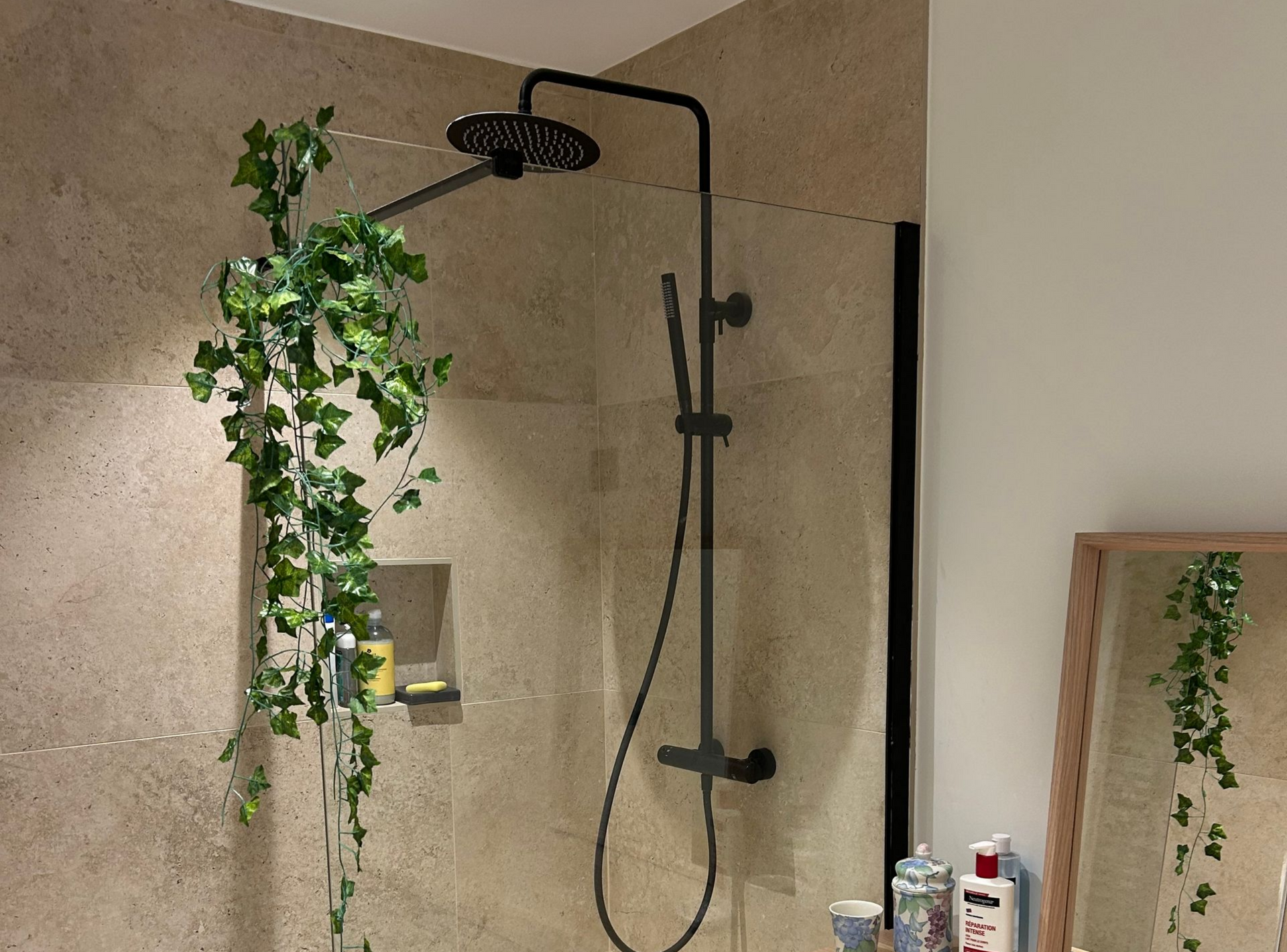 Douche avec robinetterie noire et vignes suspendues; murs carrelés beiges.