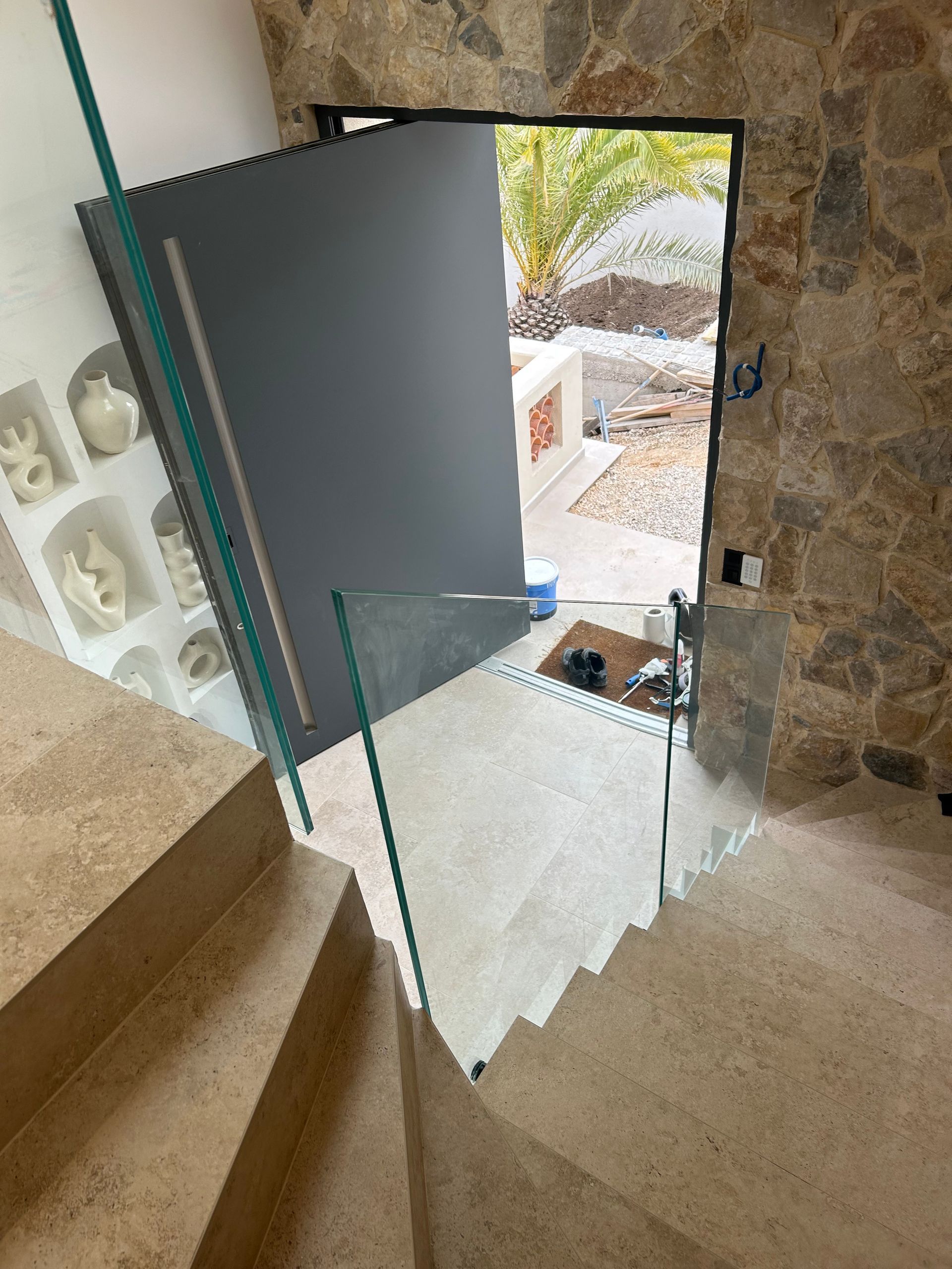 Escalier menant à une porte ouverte. On peut voir des marches en pierre et une rampe en verre.