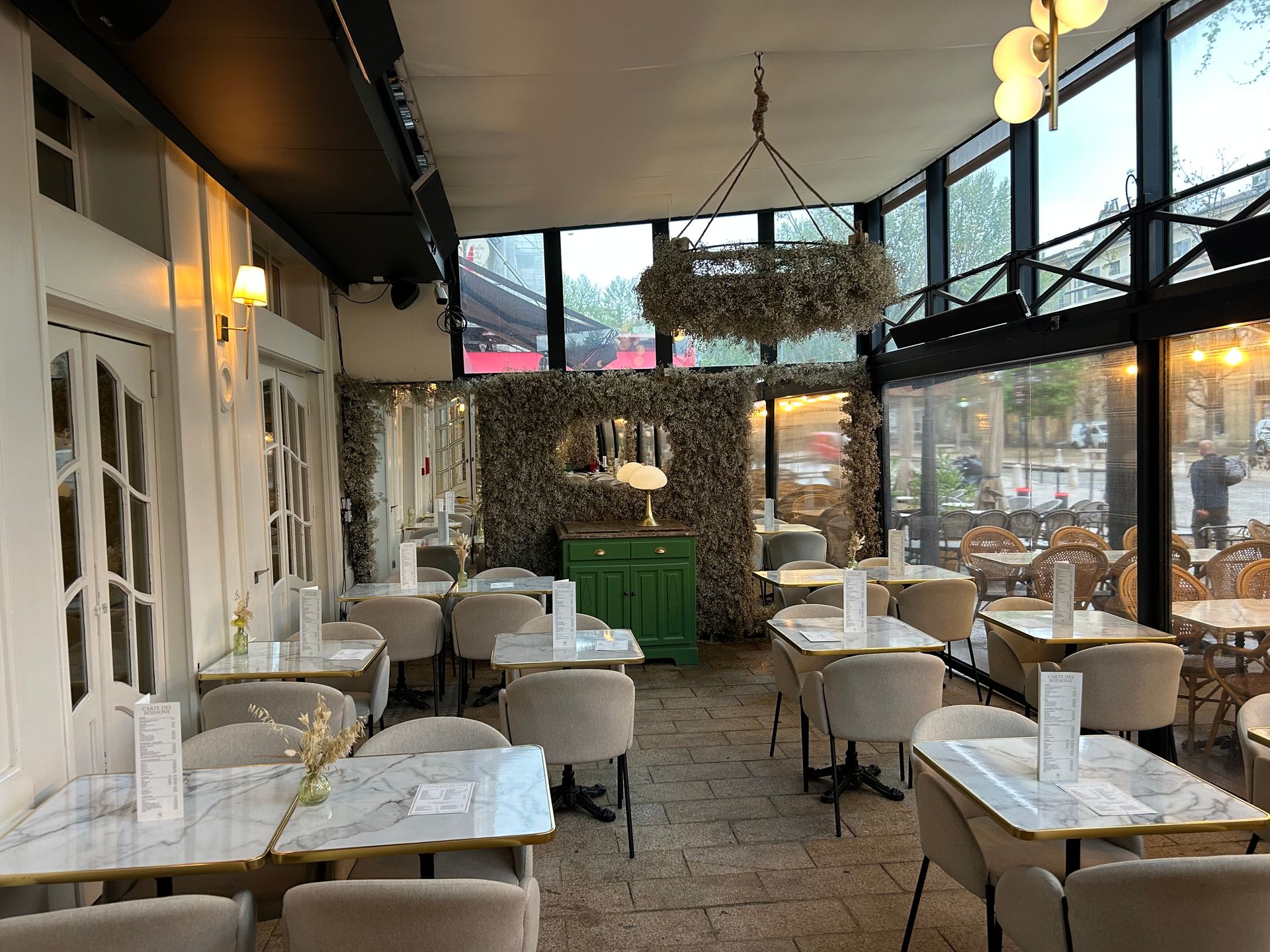 Intérieur d'un café avec tables, chaises et décoration. La lumière du soleil filtre à travers les vitres.