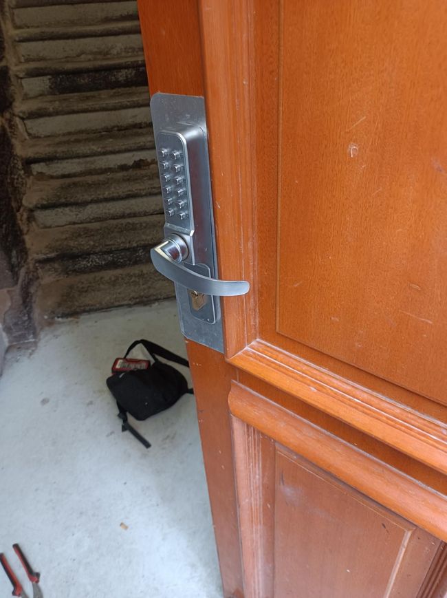 Gros plan sur une porte en bois avec une serrure à clavier argentée, donnant sur un espace en béton.