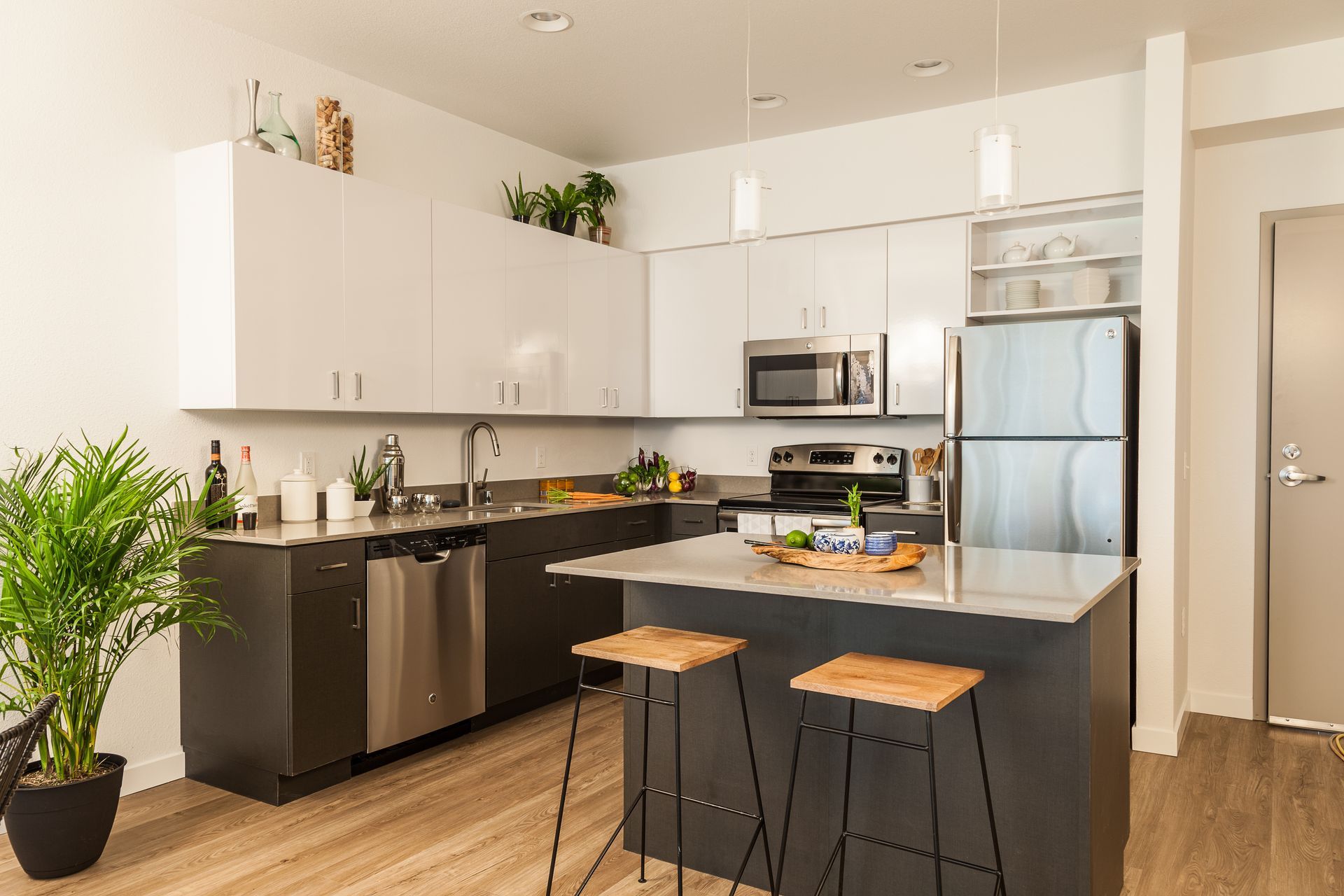 Cuisine moderne avec armoires blanches, électroménagers en acier inoxydable, îlot noir et deux tabourets.