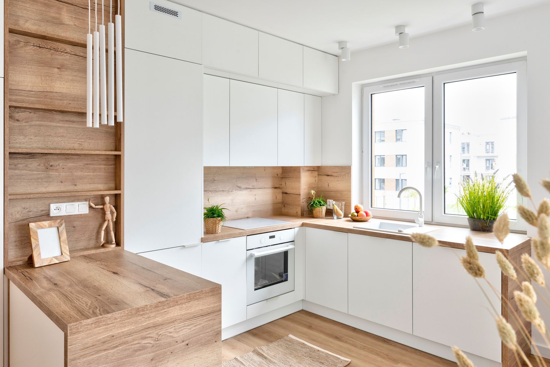 Cuisine moderne et lumineuse, blanche avec des touches de bois, de grandes fenêtres et des armoires minimalistes.