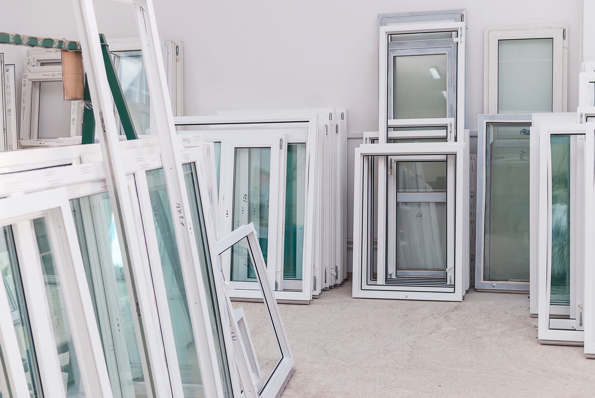 Des cadres de fenêtres blancs et des vitres empilés sont appuyés contre un mur dans un atelier lumineux.