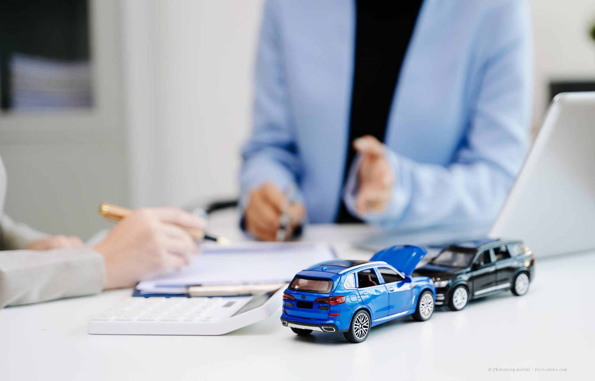 Zwei Spielzeugautos und Leute, die auf einem Schreibtisch Unterlagen durchgehen.