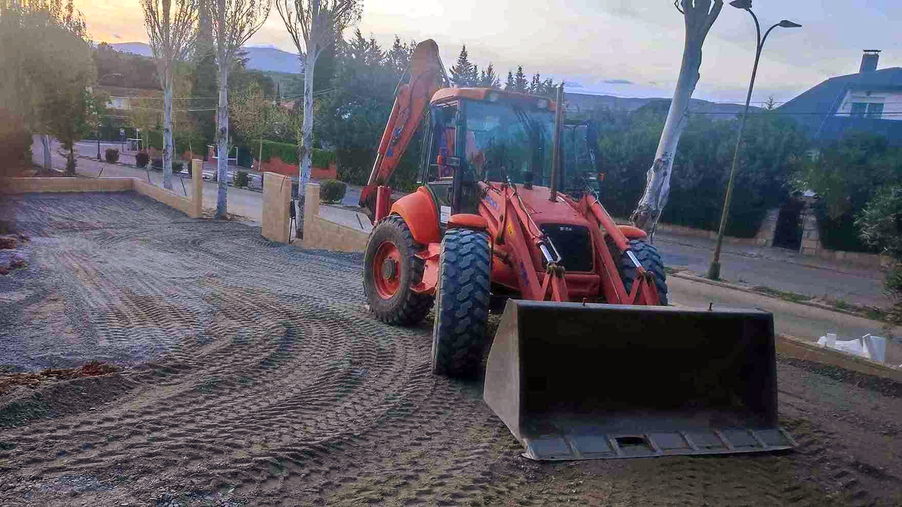 Retroexcavadora naranja en un camino de grava, preparando un terreno para la construcción. Luz del atardecer, zona residencial.
