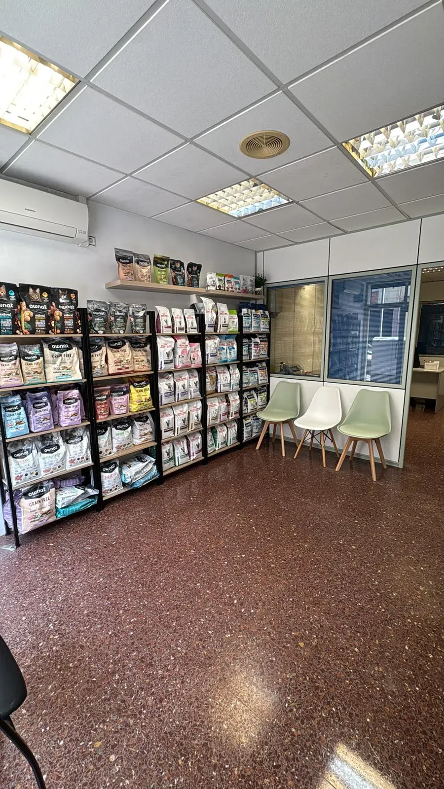 Interior de una pequeña tienda con estantes para tarjetas de felicitación, sillas blancas y luces fluorescentes brillantes en el techo.