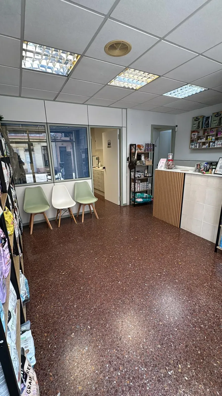 Zona de espera con sillas blancas, escritorios y un mostrador de recepción en un luminoso interior de oficina.