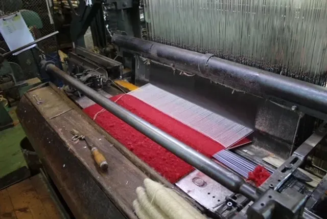 Un telar industrial con tela de color rojo brillante e hilos blancos visibles durante el proceso de producción.