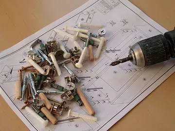Un taladro está colocado encima de un trozo de papel con tornillos y clavos.