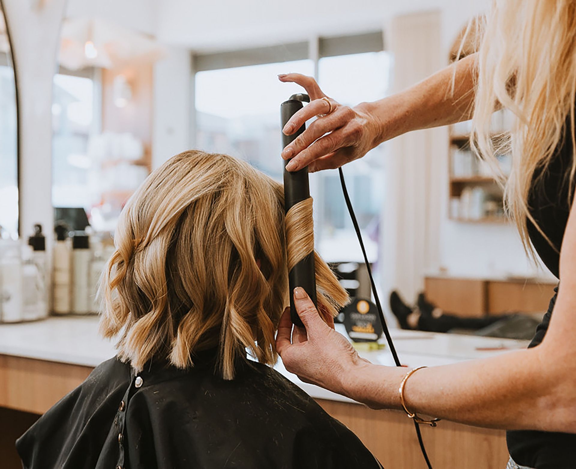 Peluquera rizando el cabello rubio de una clienta en un salón de belleza.