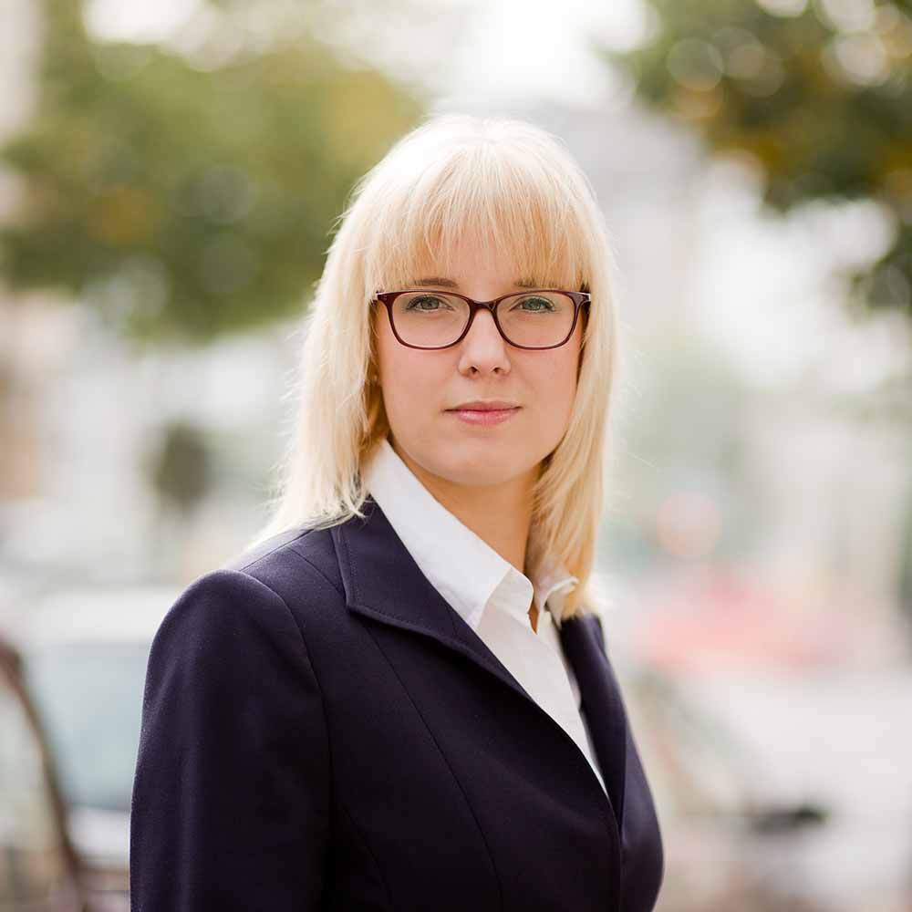 Eine Frau mit Brille und Anzug schaut in die Kamera.