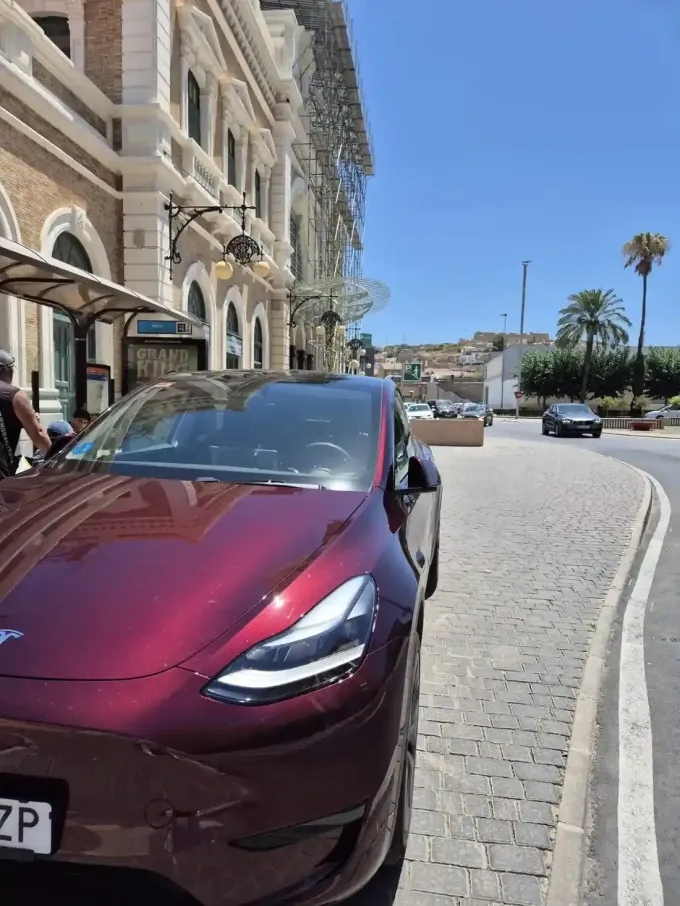 Una pareja vestida de gala sale de un lujoso coche negro en un evento nocturno al aire libre con arreglos florales de fondo.