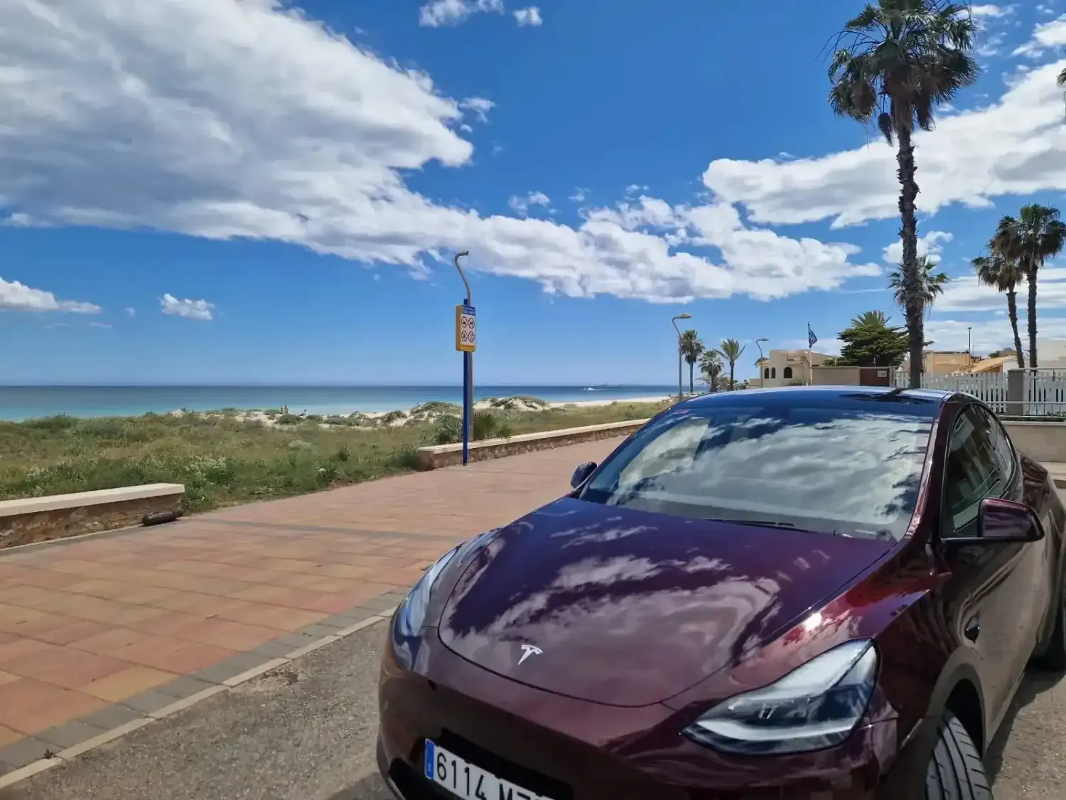 Una persona sonriente vestida con traje se encuentra de pie frente a un elegante Tesla negro estacionado en una calle.