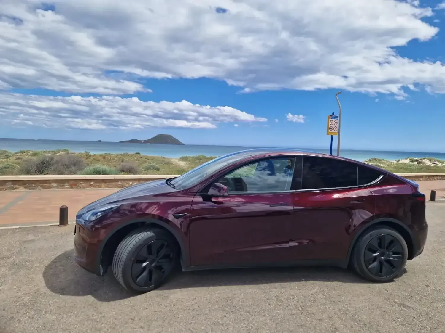 Un conductor con traje está de pie junto a un Tesla gris a las afueras de una terminal de aeropuerto.