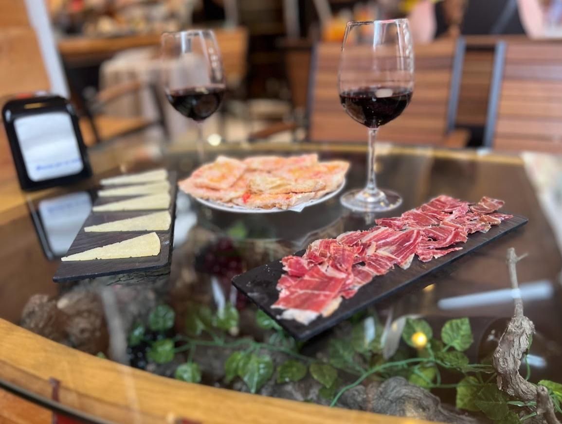 Una mesa de cristal sobre la que hay un plato de carne y dos copas de vino.
