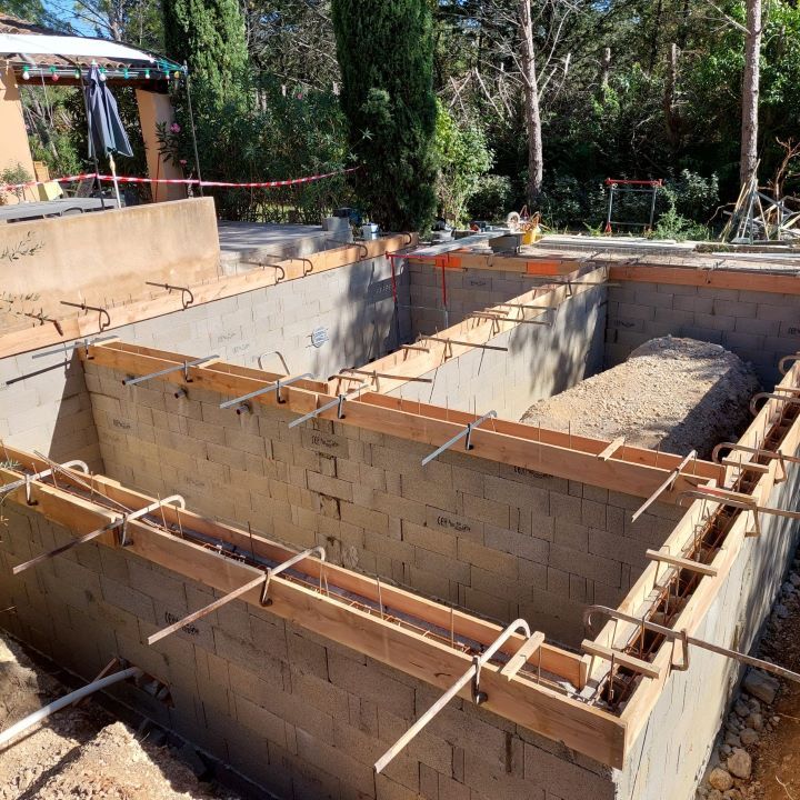 Construction d'une coque de piscine en béton avec coffrages en bois et armatures métalliques en extérieur.